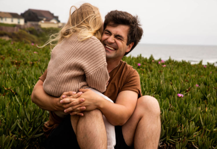 A young single father enjoying a special moment with his daughter at the beach, enveloping her in his arms.