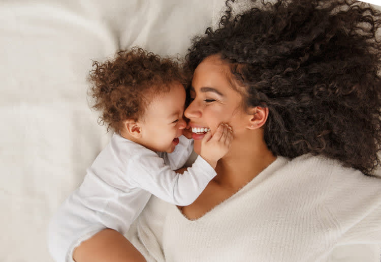 Smiling baby and mom lying on the bed.
