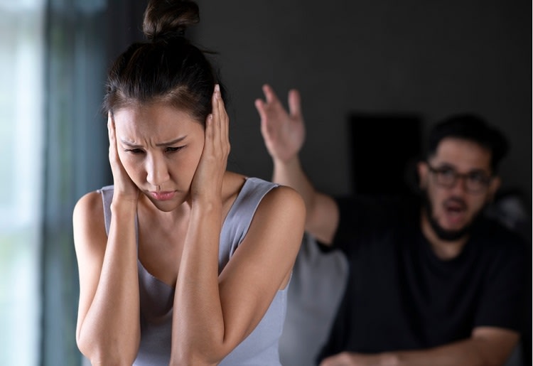 Woman covering her ears and looking away from man pointing and shouting