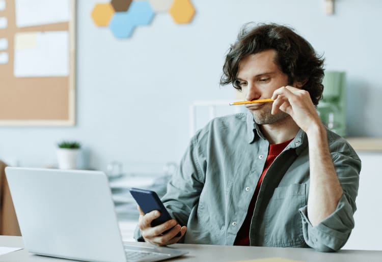 a man sitting in front of a laptop computer while holding a pencil in his mouthHow to Stop Procrastination and Boost Productivity 