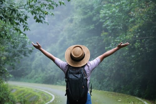 A woman standing on a road in a forest with her arms spread out wide  happily